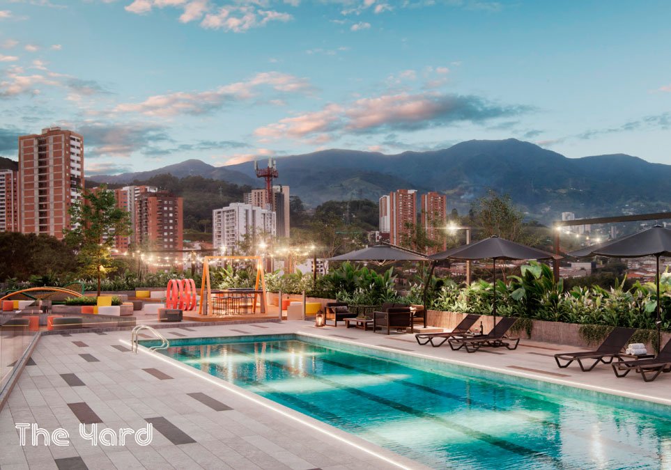 Render de la piscina y zona social del proyecto Vitral Medellín The Yard, con vista a la ciudad y a las montañas.